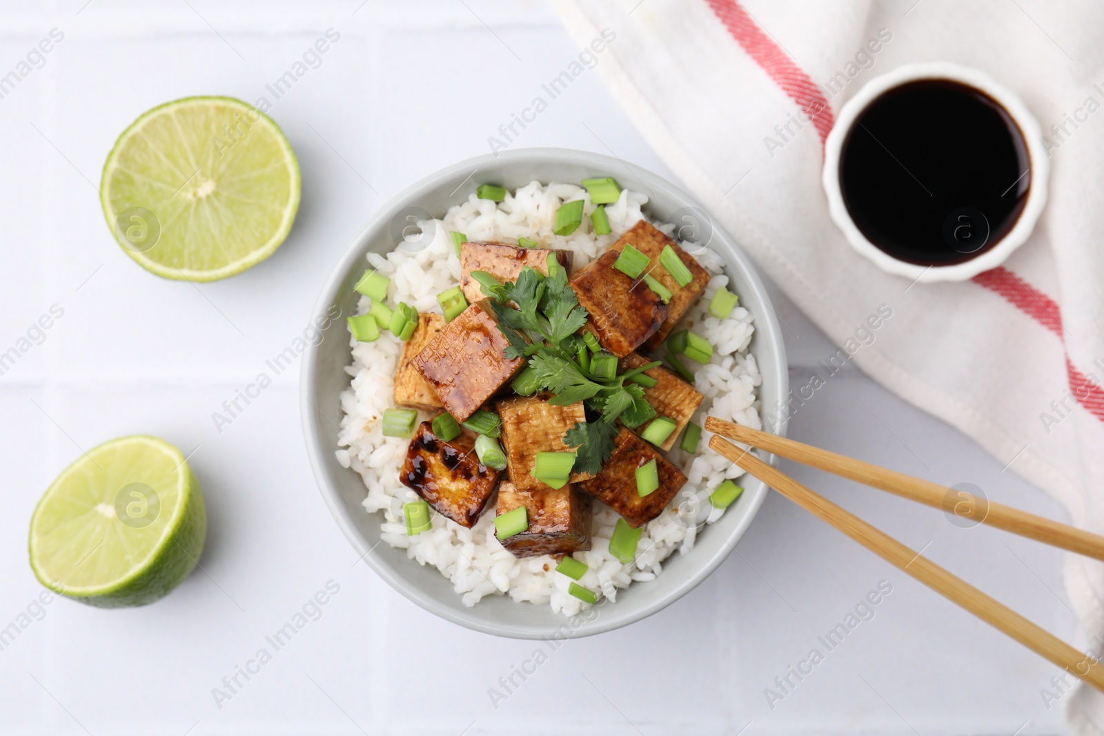 Photo of Delicious rice with fried tofu and greens served on white tiled table, flat lay