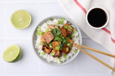 Delicious rice with fried tofu and greens served on white tiled table, flat lay