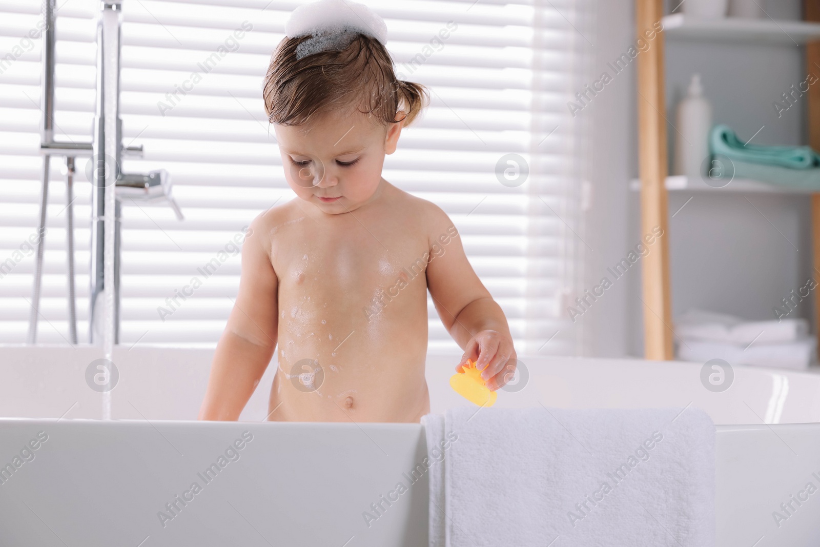 Photo of Cute little girl taking bath with toy indoors