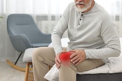 Senior man suffering from pain in knee at home, closeup