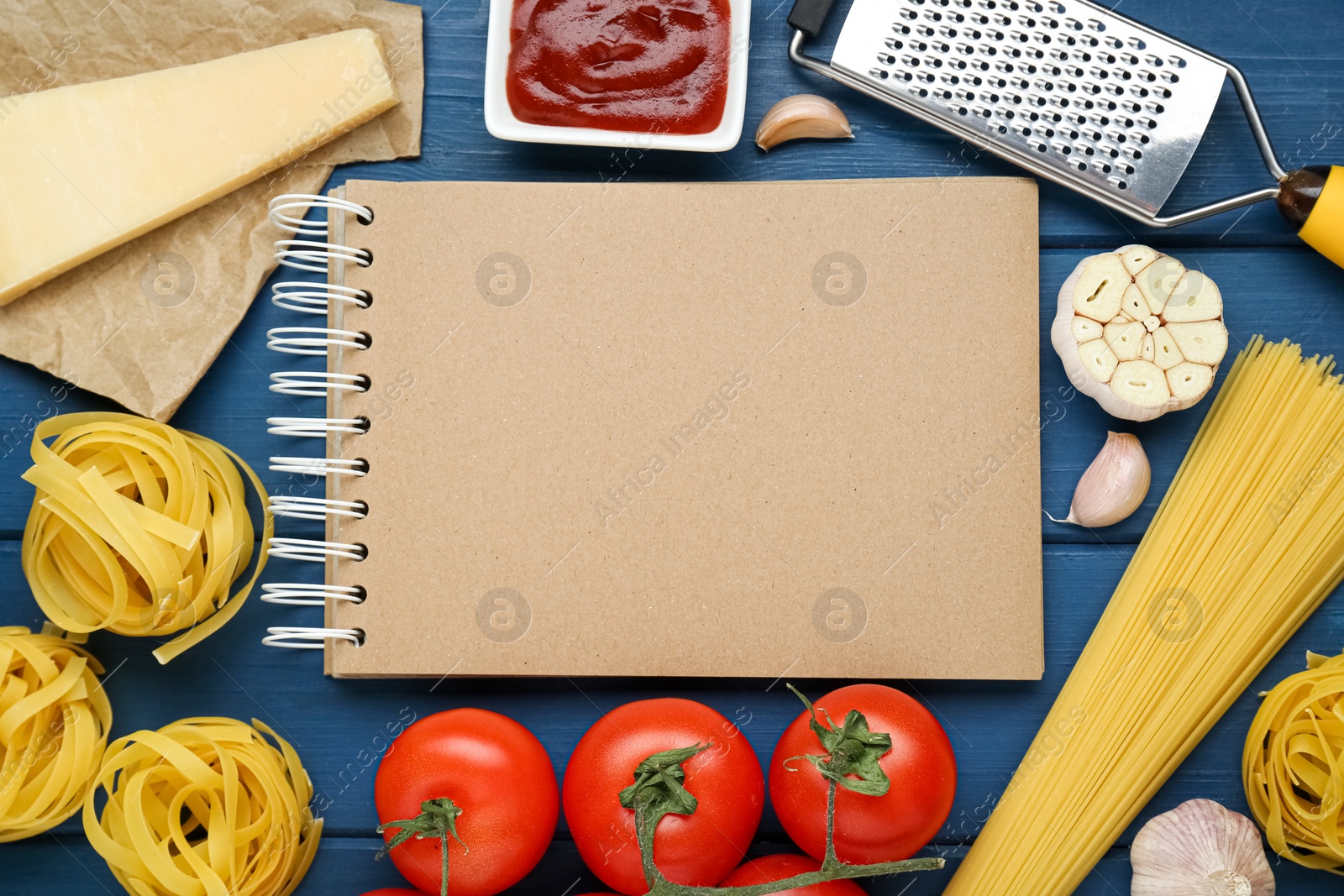 Photo of Blank recipe book surrounded by different ingredients on blue wooden table, flat lay. Space for text