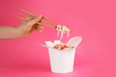 Photo of Woman eating vegetarian wok noodles with chopsticks from box on pink background, closeup