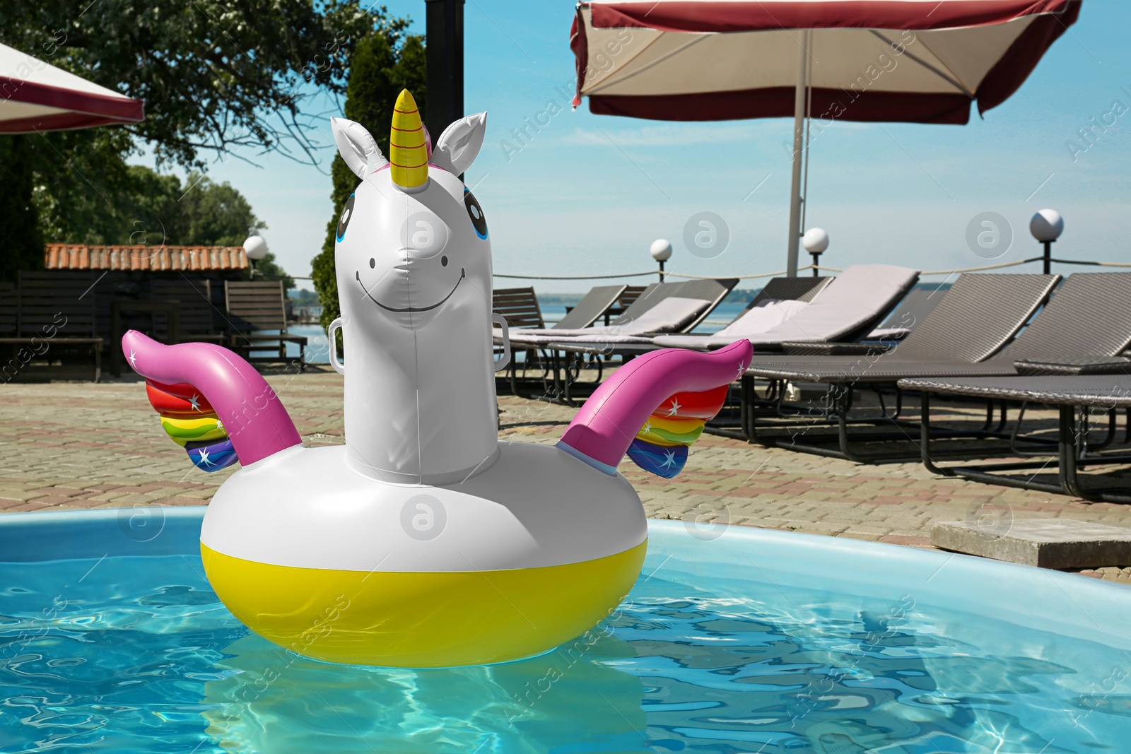 Photo of Funny inflatable unicorn ring floating in swimming pool on sunny day, outdoors. Space for text
