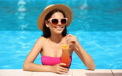 Photo of Beautiful young woman with cocktail in blue swimming pool