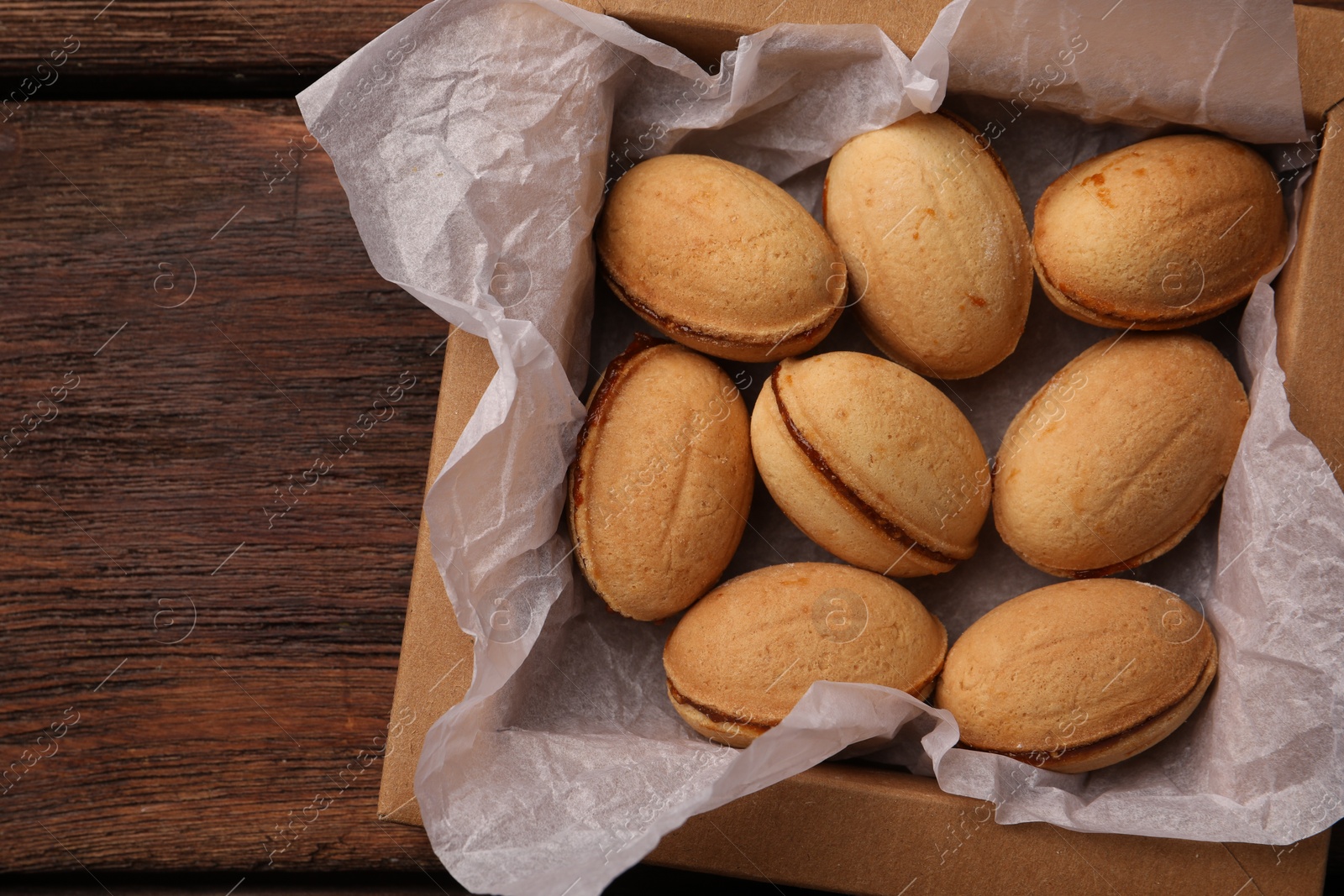 Photo of Delicious nut shaped cookies with boiled condensed milk in box on wooden table, top view