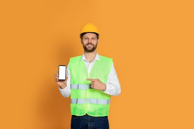 Man in reflective uniform showing smartphone on orange background
