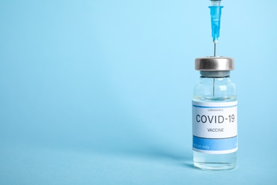 Filling syringe with coronavirus vaccine on light blue  background, space for text