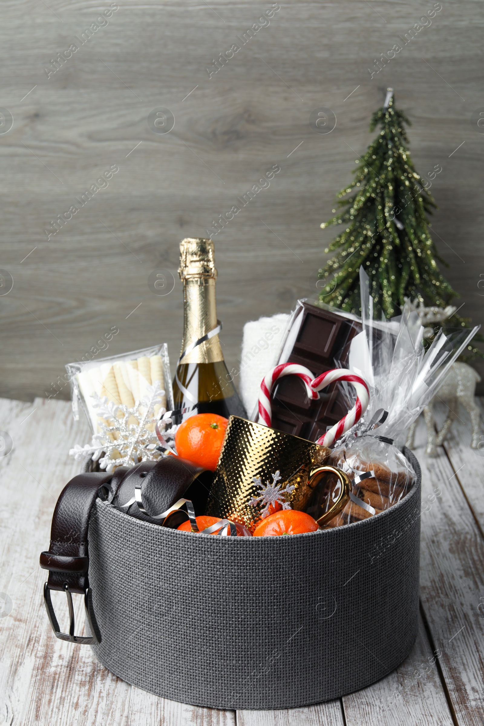 Photo of Christmas gift basket with champagne, candy canes and tangerines on white wooden table