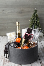 Christmas gift basket with champagne, candy canes and tangerines on white wooden table