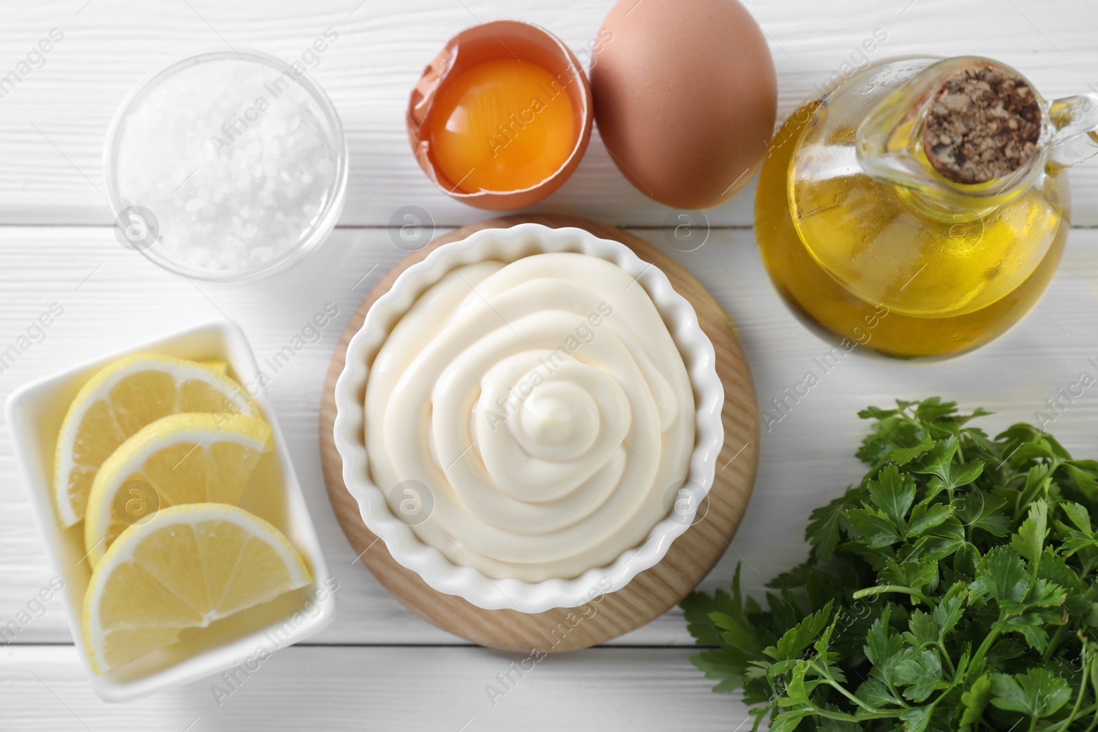 Photo of Fresh mayonnaise sauce in bowl and ingredients on white wooden table, flat lay