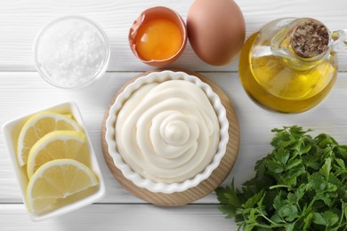 Photo of Fresh mayonnaise sauce in bowl and ingredients on white wooden table, flat lay