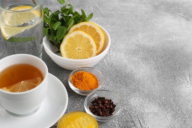 Cup with delicious immunity boosting tea and ingredients on grey table, space for text