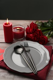 Photo of Romantic place setting with red roses and candles on wooden table. St. Valentine's day dinner