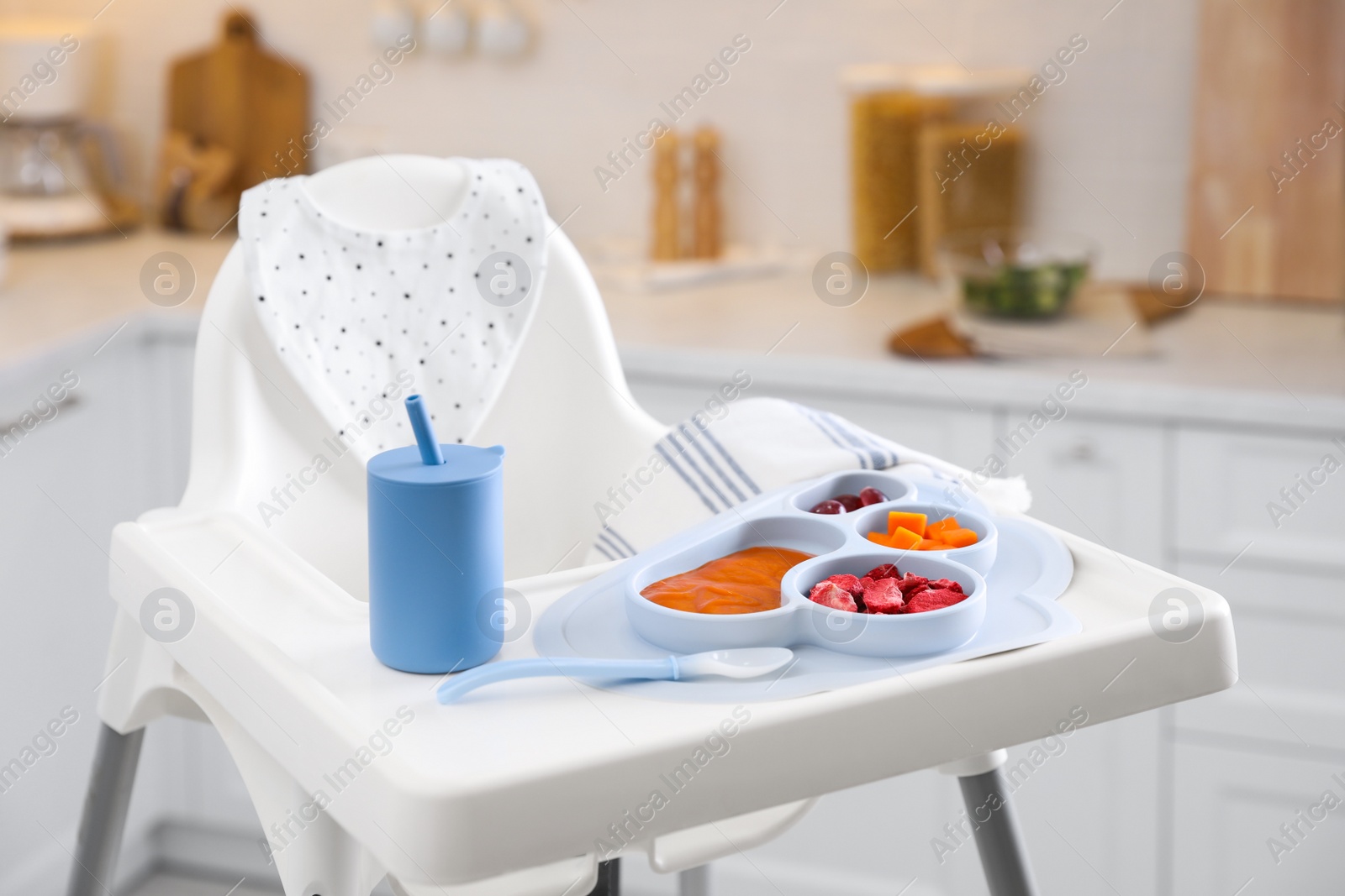 Photo of High chair with food in baby tableware on white tray indoors