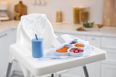 High chair with food in baby tableware on white tray indoors