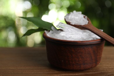Photo of Bowl and spoon with menthol crystals on wooden table against blurred background