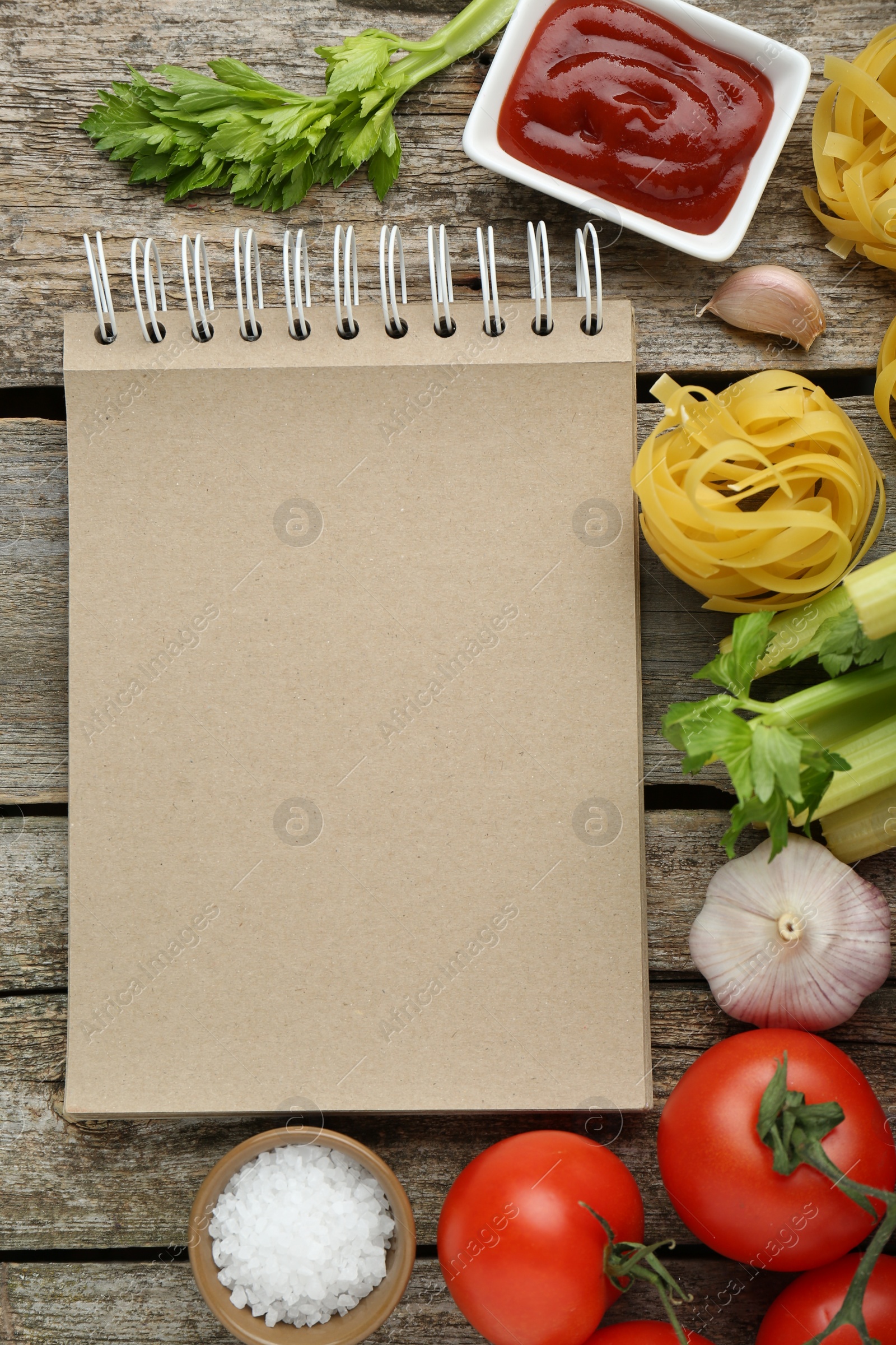 Photo of Blank recipe book and different ingredients on wooden table, flat lay. Space for text