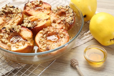 Delicious baked quinces with nuts in bowl, honey and fresh fruits on wooden table, closeup