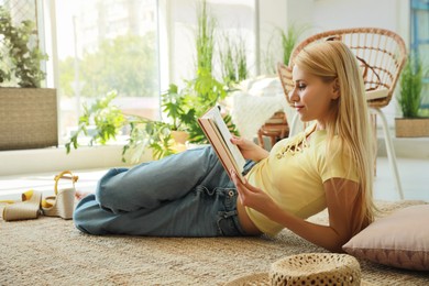 Happy young woman reading book on floor at indoor terrace