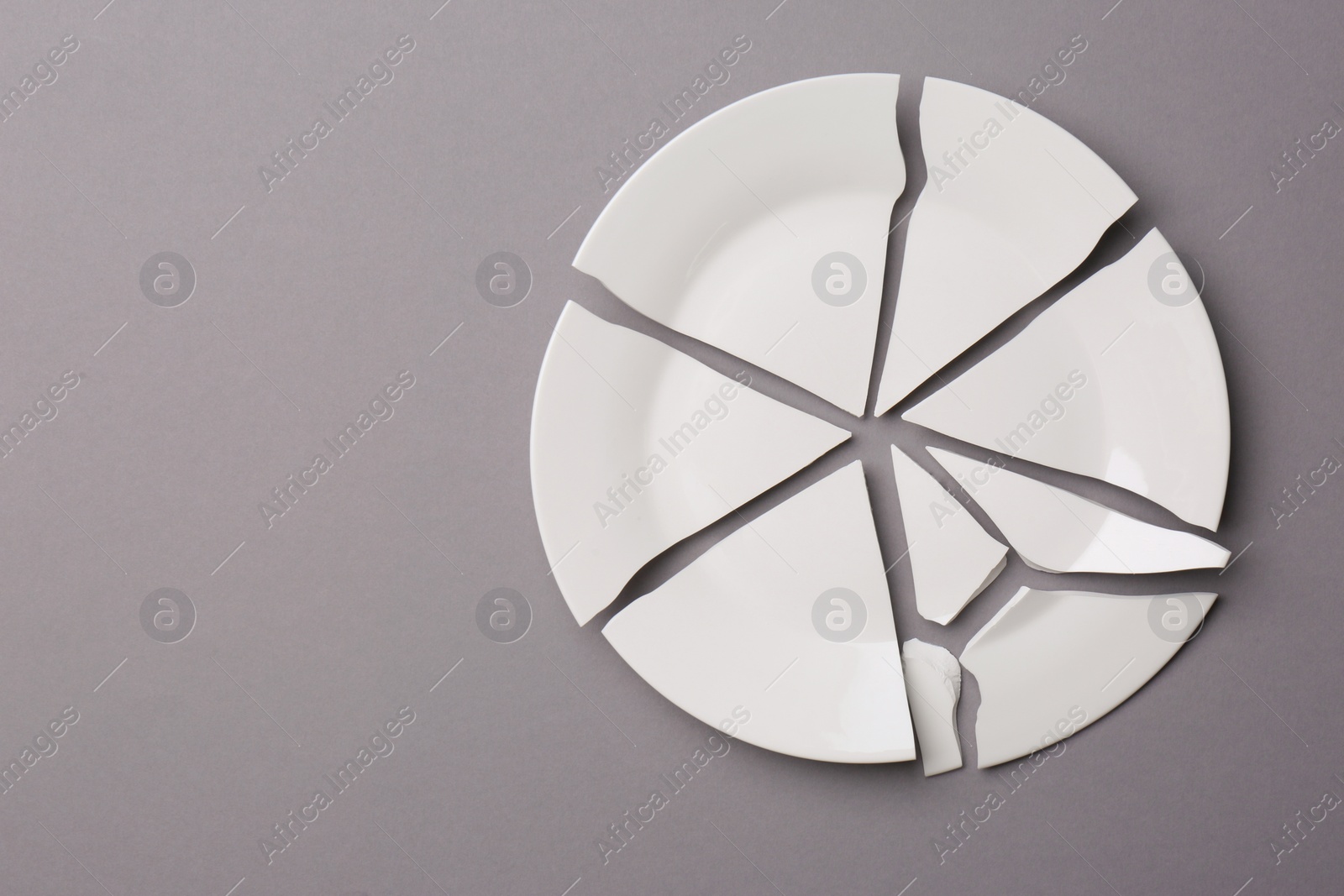Photo of Pieces of broken white ceramic plate on grey background, top view. Space for text