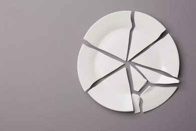 Pieces of broken white ceramic plate on grey background, top view. Space for text