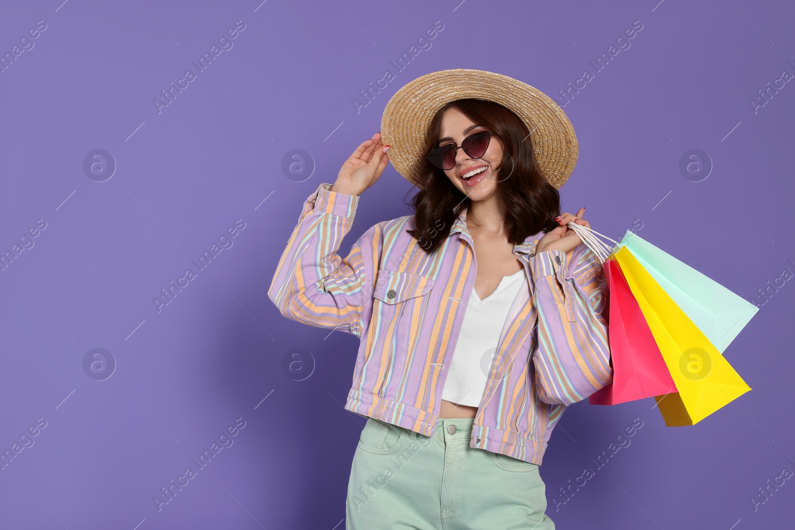Photo of Beautiful young woman with paper shopping bags on purple background. Space for text