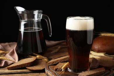 Photo of Composition with delicious kvass, spikes and bread on wooden table against black background