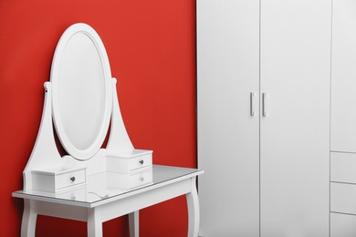 Elegant white makeup table near red wall