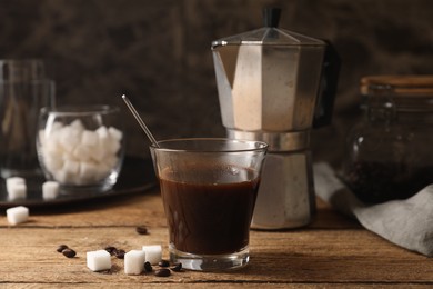 Photo of Brewed coffee in glass, moka pot, beans and sugar cubes on wooden table