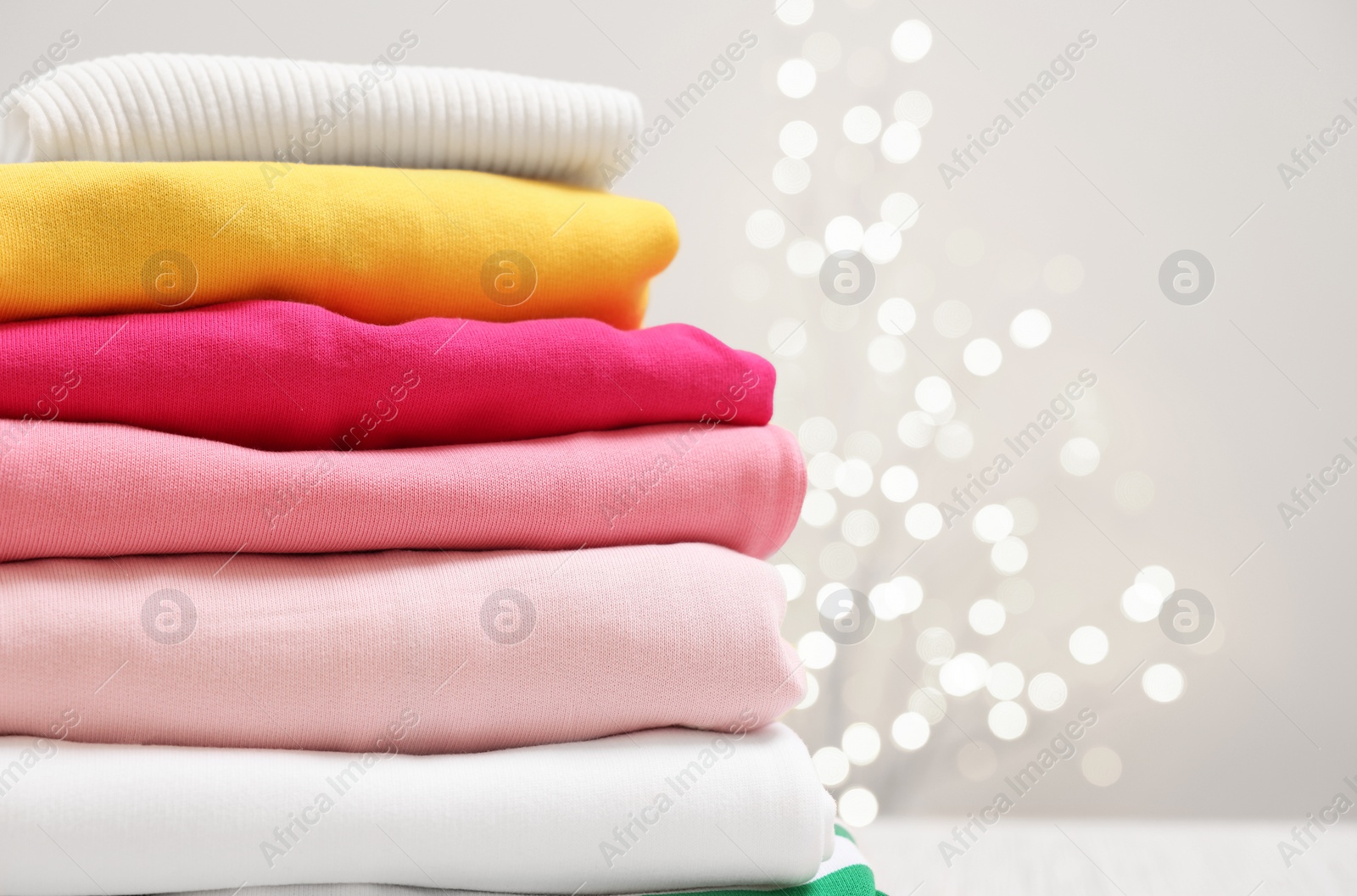 Stack of folded clothes on beige background with blurred lights, closeup. Space for text Photo of Stack of folded clothes on beige background with blurred lights, closeup. Space for text