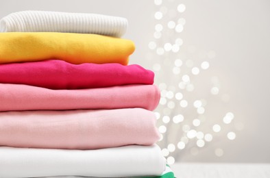 Photo of Stack of folded clothes on beige background with blurred lights, closeup. Space for text