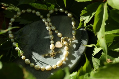 Photo of Stylish presentation of elegant pearl necklace on stone stand outdoors