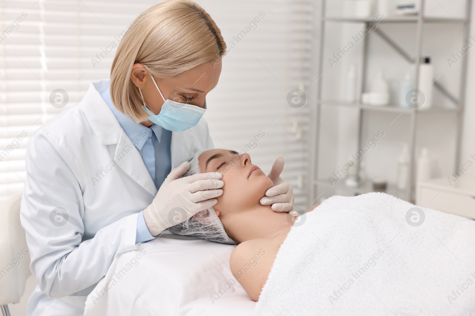 Photo of Dermatologist in medical mask examining patient`s face in clinic