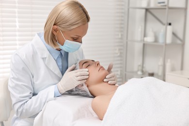 Dermatologist in medical mask examining patient`s face in clinic