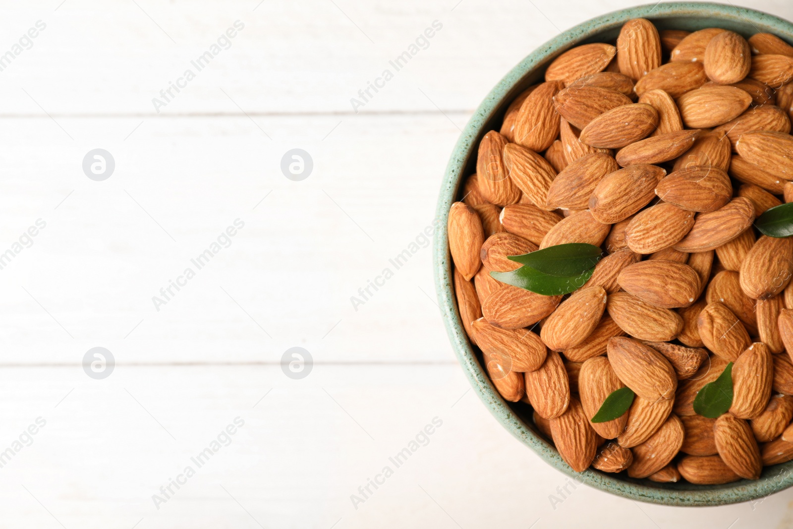 Photo of Tasty organic almond nuts in bowl and space for text on table, top view