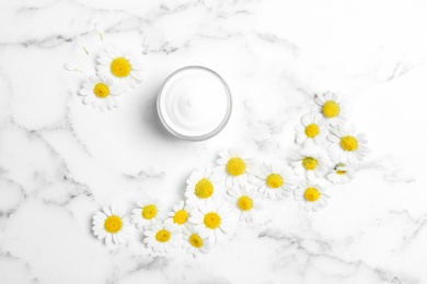 Photo of Chamomile flowers and jar of cream on white marble table, flat lay