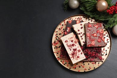 Photo of Different chocolate bars with freeze dried fruits and Christmas decor on black table, flat lay. Space for text