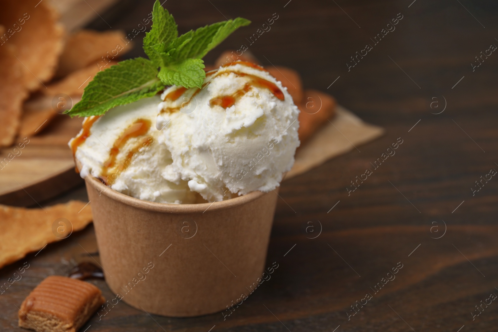 Photo of Scoops of tasty ice cream with caramel sauce, mint and candies on wooden table, closeup. Space for text