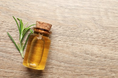 Bottle with essential oil and fresh rosemary on wooden table, top view. Space for text