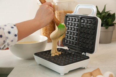 Photo of Woman pouring dough onto Belgian waffle maker in kitchen, closeup