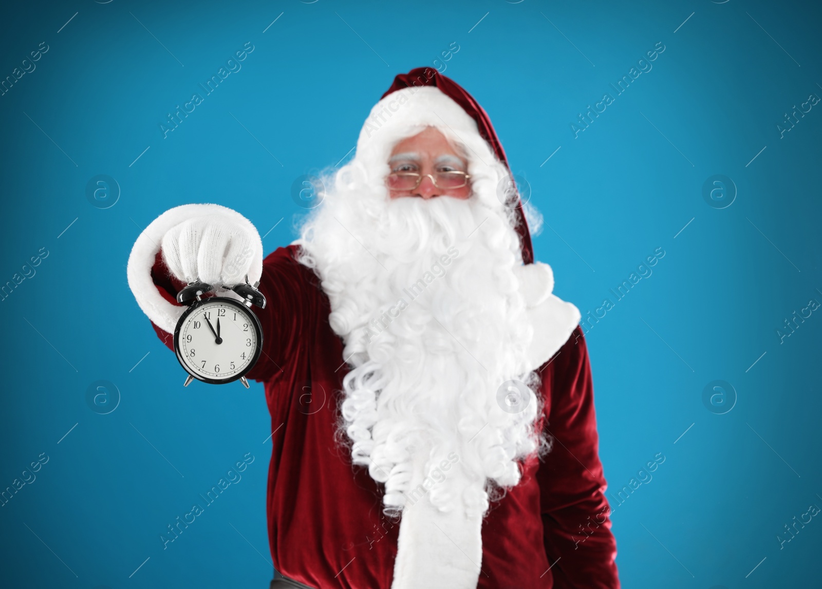 Photo of Santa Claus holding alarm clock on blue background. Christmas countdown