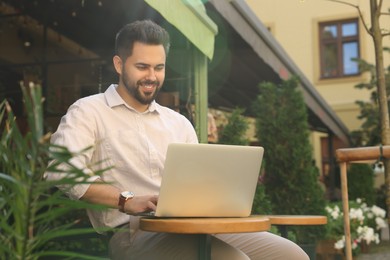 Photo of Handsome young man working on laptop at table in outdoor cafe