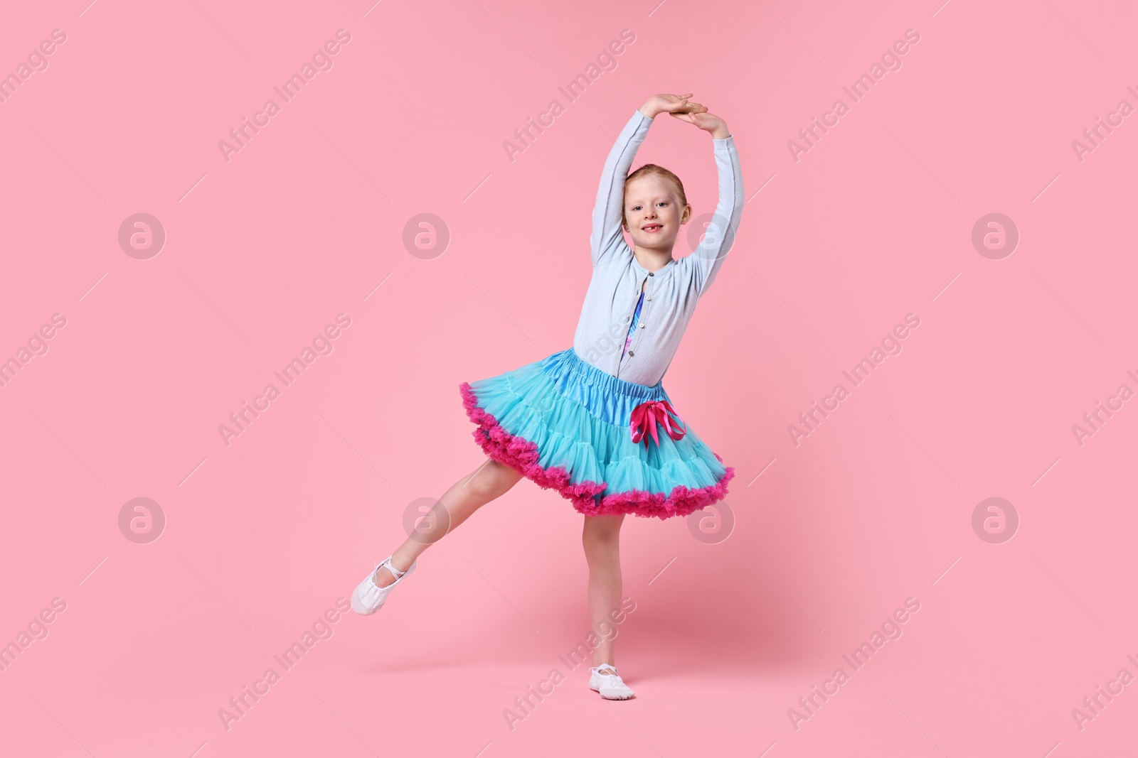 Photo of Cute little girl dancing on pink background