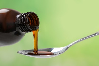 Pouring syrup from bottle into spoon against light green background, closeup. Cold medicine