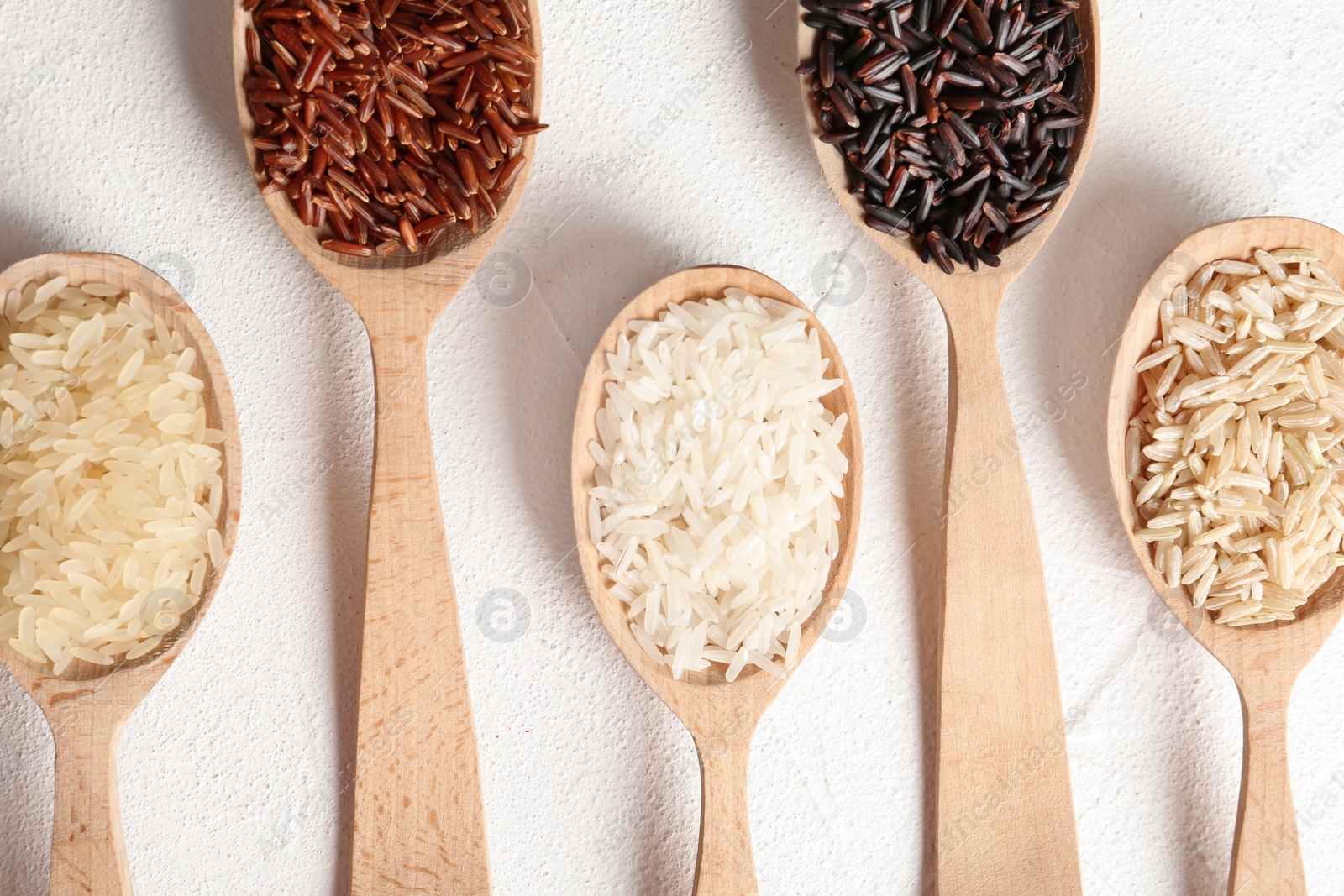 Photo of Flat lay composition with brown and other types of rice in spoons on white background