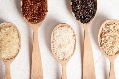 Photo of Flat lay composition with brown and other types of rice in spoons on white background
