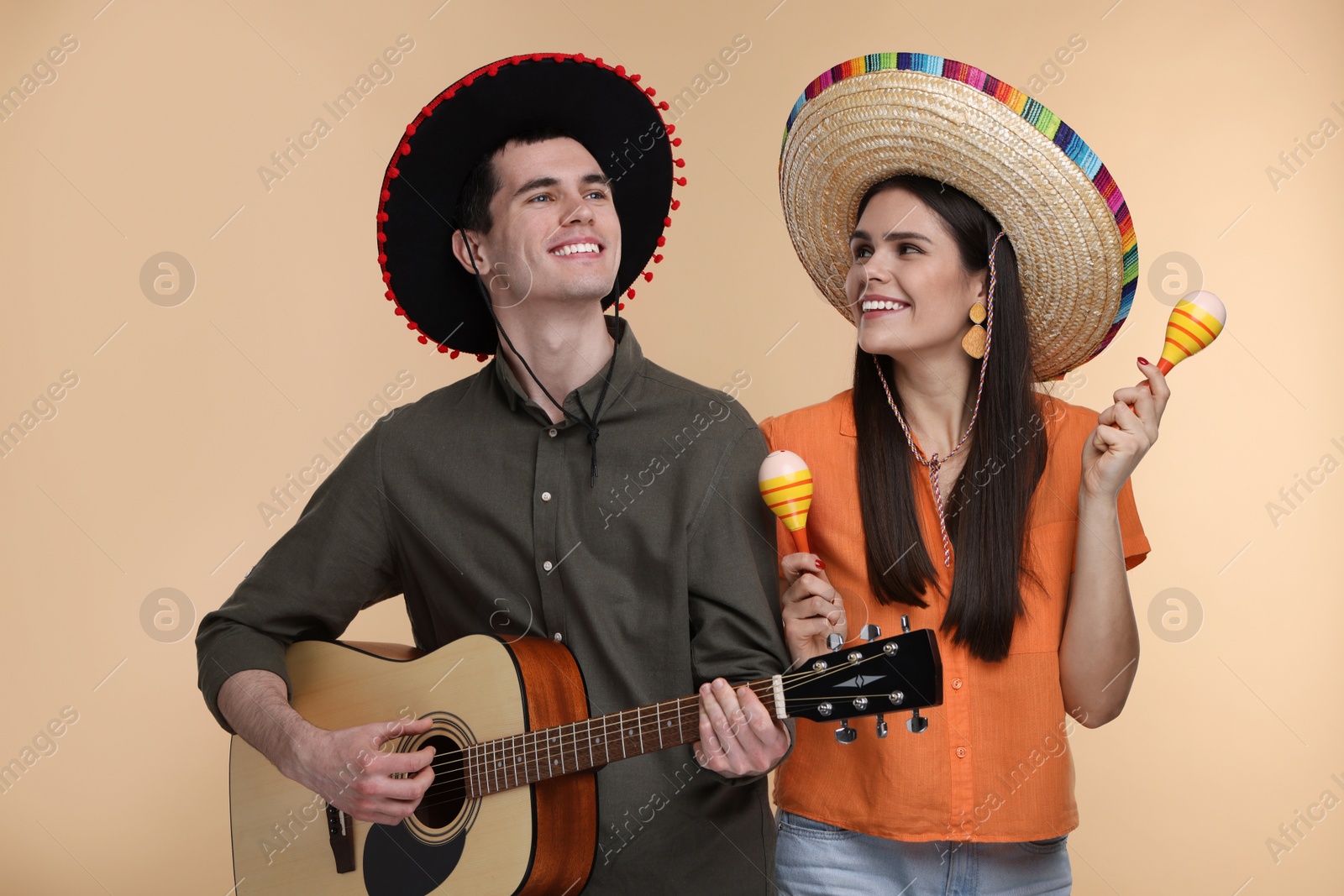 Photo of Lovely couple woman in Mexican sombrero hats with maracas and guitar on beige background