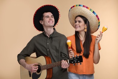 Photo of Lovely couple woman in Mexican sombrero hats with maracas and guitar on beige background