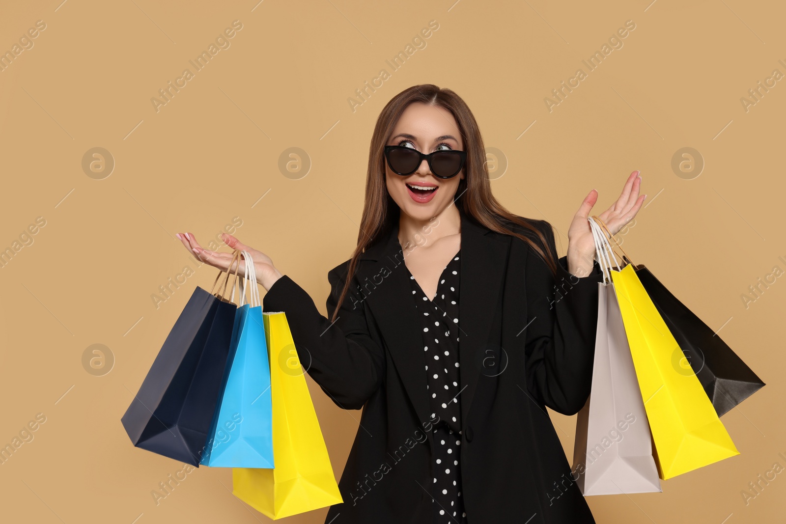 Photo of Stylish young woman in sunglasses with shopping bags on beige background