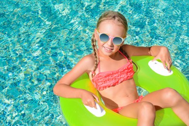 Photo of Cute little girl with sunglasses and inflatable ring in pool on sunny day